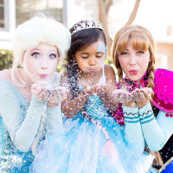 Two ice-queen party characters posing with delighted children