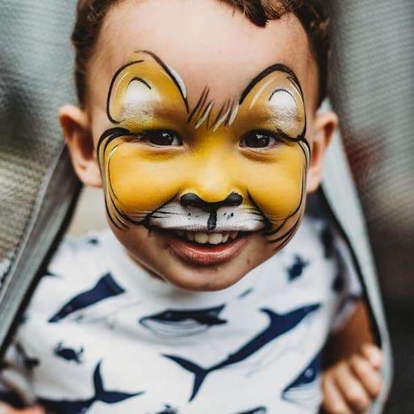 A face painter carefully painting a smiling child's cheek at a party