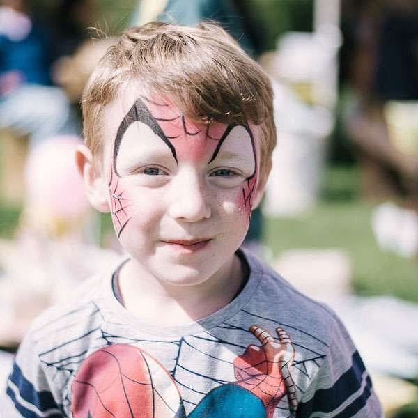 A face painter finishing a bold Spider-Man design on a smiling child