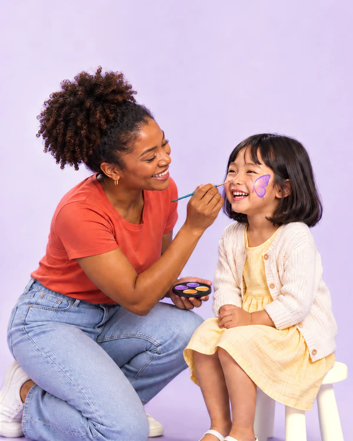 A face painter adding a lavender butterfly to a laughing girl’s cheek